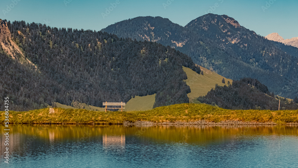 Beautiful alpine summer view with a wooden bench in the background and reflections in a lake at Fieberbrunn, Tyrol, Austria