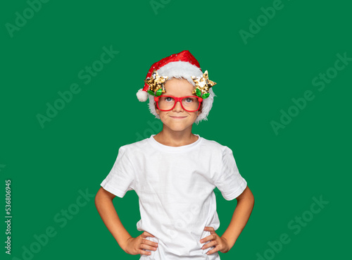 Boy in Santa Claus hat and glasses. Green background with space for text. Selective focus. Picture for articles and advertisements about children, holidays, Christmas.