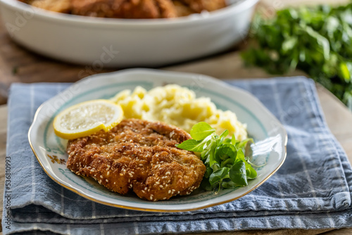 Schnitzel with sesame seeds served with potato mash and greens on a plate