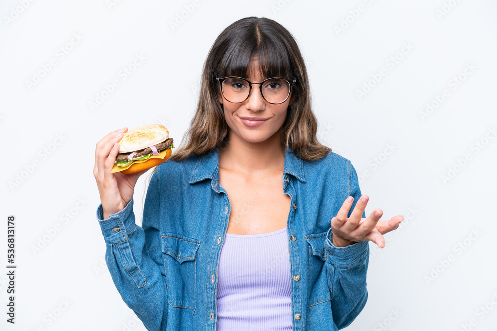 Young caucasian woman holding a burger isolated on white background making doubts gesture while lifting the shoulders Young caucasian woman holding a burger isolated on white background making doubts gesture while lifting the shoulders