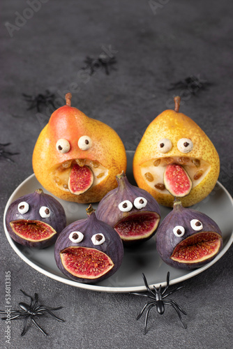 Spooky pear and fig monsters for Halloween party on gray background decorated with spiders and bats, Halloween Fruit Serving Idea