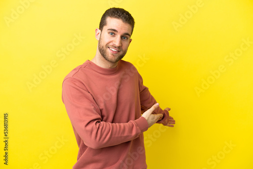 Quadro su tela Handsome blonde man over isolated yellow background extending hands to the side