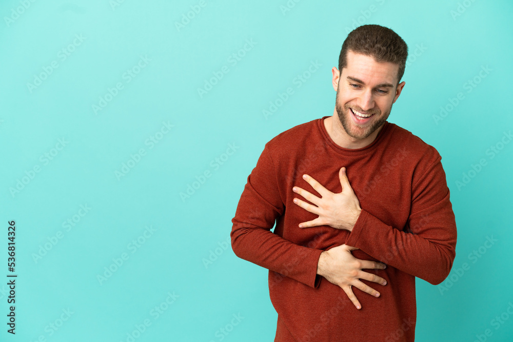 Handsome blonde man over isolated blue background smiling a lot