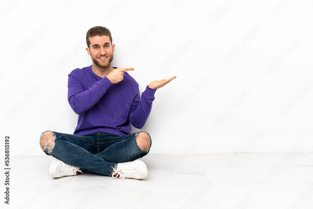 Young man sitting on the floor holding copyspace imaginary on the palm to insert an ad Young man sitting on the floor holding copyspace imaginary on the palm to insert an ad