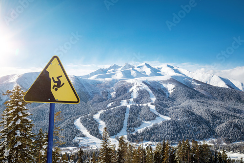 Yellow warning sign at a ski resort, ski slopes in the background