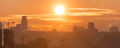 Panoramic view of sunset in the city with silhouette of buildings and industrial cranes