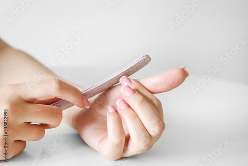 A girl with beautiful long nails makes a manicure with a nail file on a white background, close up of hands