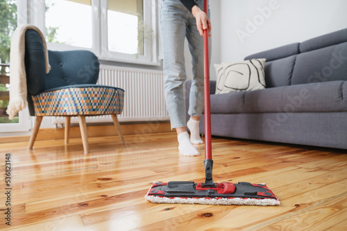 woman cleaning wooden floor with mop in living room