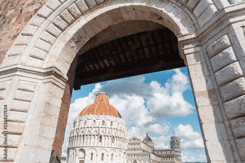 Fototapeta premium Beautiful vintage wall with an archway overlooks famous landmarks with towers, ancient buildings and a Renaissance church in Pisa, Italy. Traveling in Europe