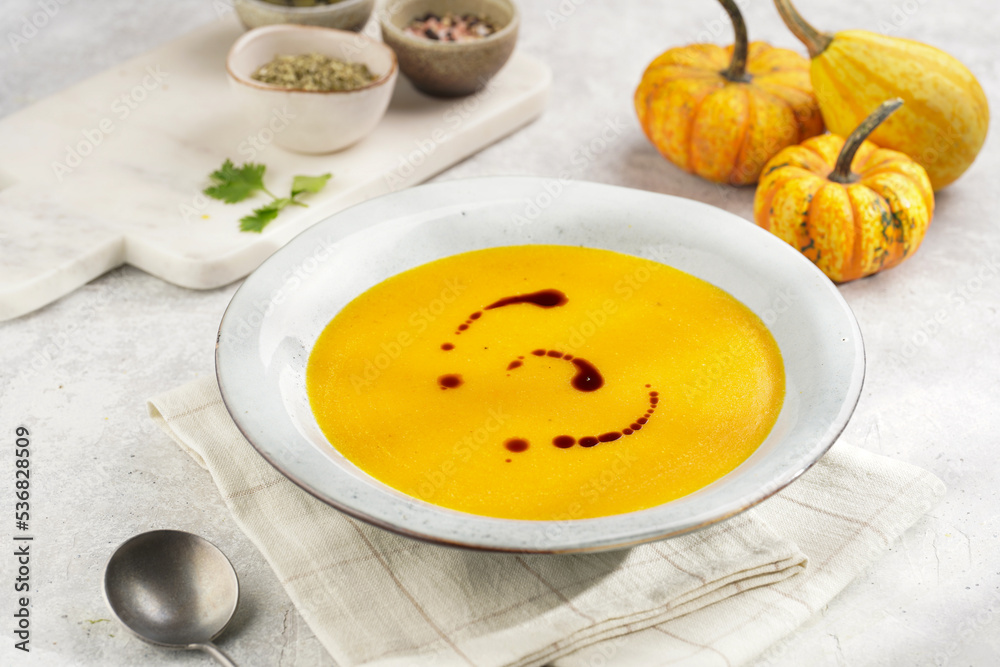 One deep grey soup bowl with an orange pumpkin cream soup with pumpkin seed oil, on a gray concrete background One deep grey soup bowl with an orange pumpkin cream soup with pumpkin seed oil, on a gray concrete background