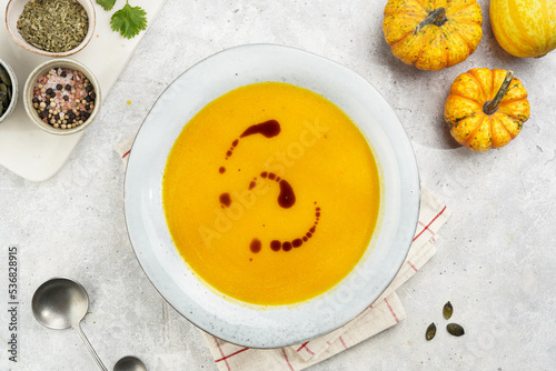 One deep grey soup bowl with an orange pumpkin cream soup with pumpkin seed oil, on a gray concrete background, top view