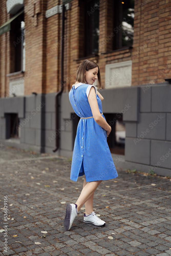 Naklejka premium Happy pregnant woman chilling and having fun while walking in the city in a midi blue vintage dress. Happiness all around