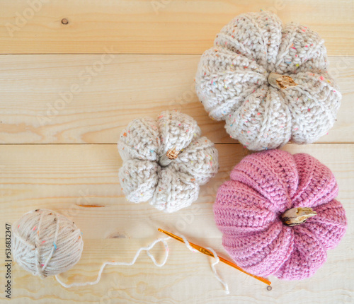 beige and soft pink colored crochet woolen pumpkins on wooden ground with crochet hook and woolen ball