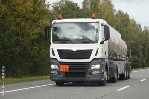 Obraz na płótnie White semi truck barrel truck with 30-1202 dangerous goods class sign drive on suburban highway road at autumn day, front view, diesel fuel ADR cargo transportation logistics w salonie