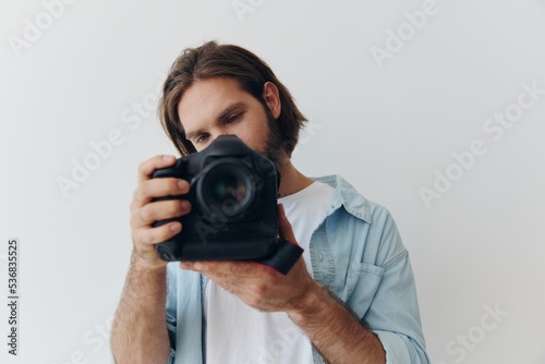 Man hipster photographer in a studio against a white background holding a professional camera and setting it up before shooting. Lifestyle work as a freelance photographer