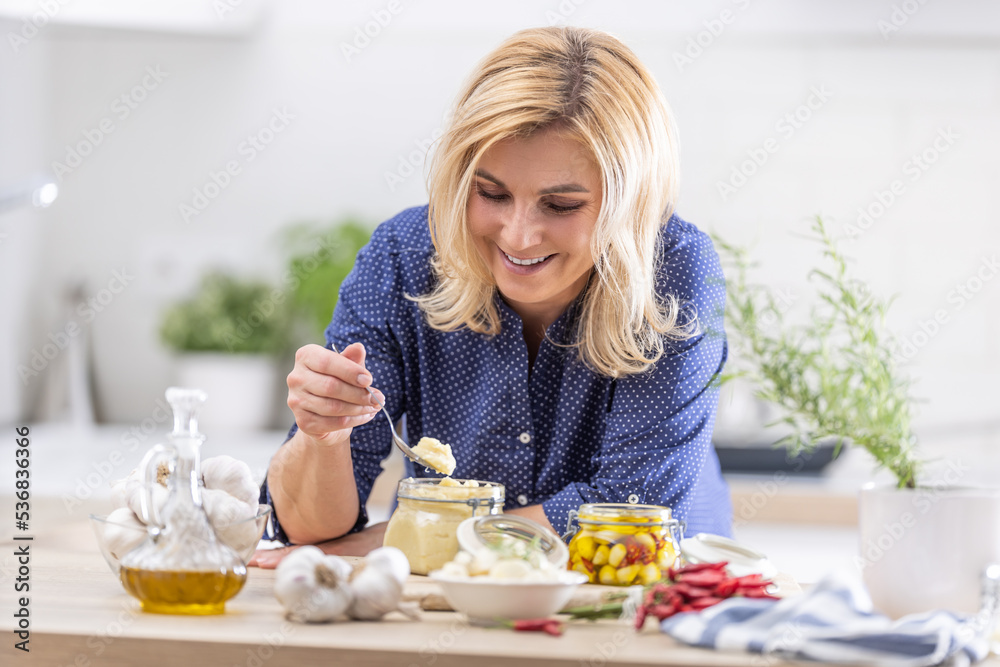 Smiling blonde woman takes spoonful of crushed garlic during preserves making session in the autumn Smiling blonde woman takes spoonful of crushed garlic during preserves making session in the autumn