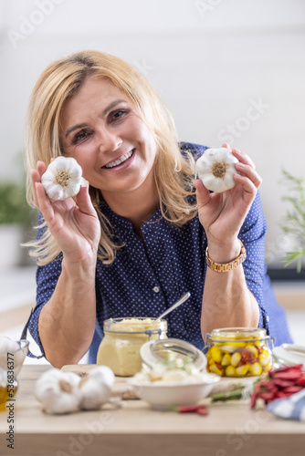 Happy woman takes garlic heads and makes them into preserves in the kitchen