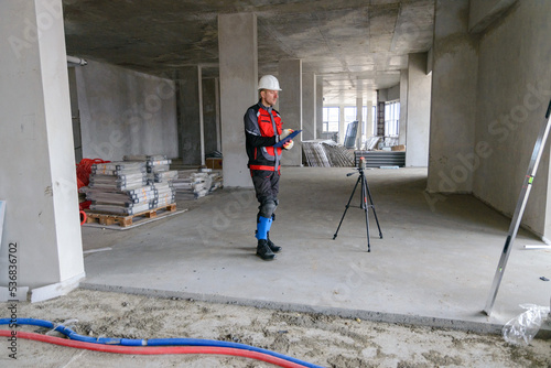 A foreman at a construction site in work clothes controls the work process, takes the necessary measurements