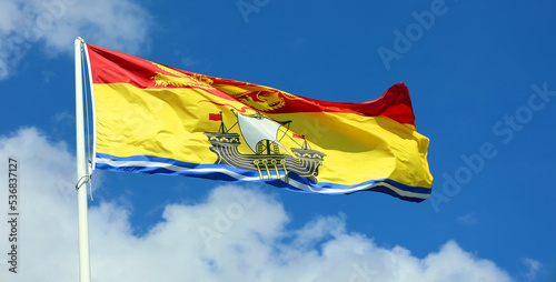 The flag of New Brunswick consists of a golden lion passant on a red field in the upper third and a gold field defaced with a lymphad on top of blue and white wavy lines in the bottom two-thirds. photo