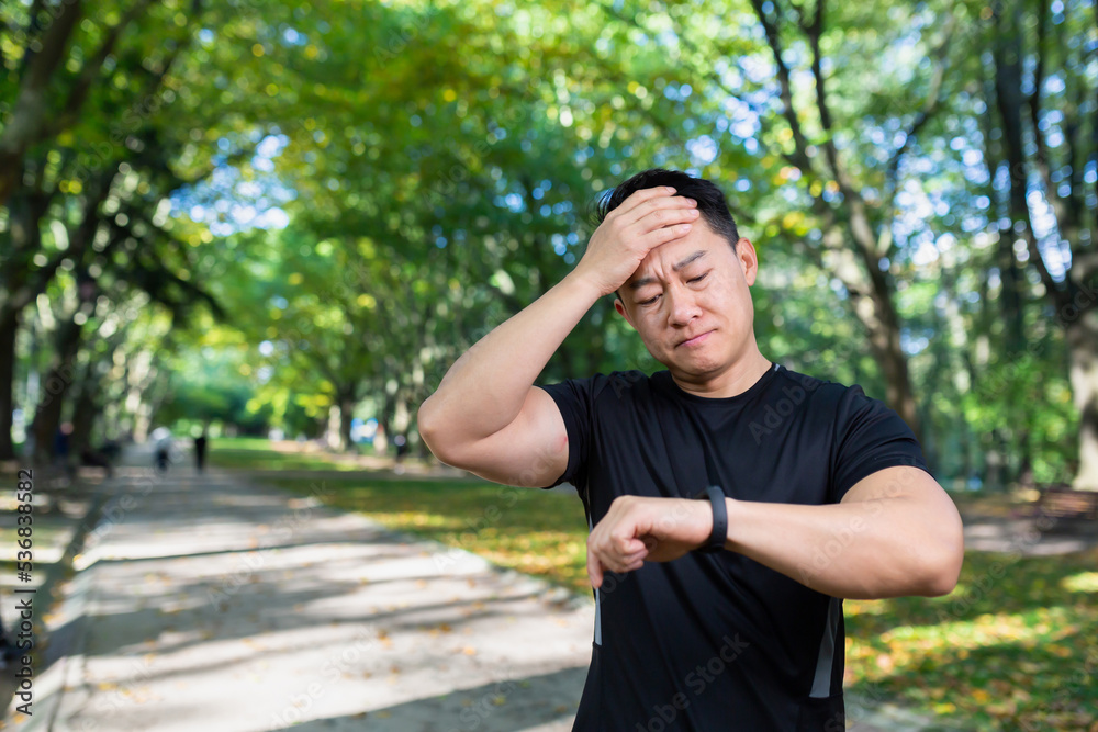 unhappy and upset male athlete looking at fitness with smartwatch, bad workout result, asian man exercising in autumn park on day. unhappy and upset male athlete looking at fitness with smartwatch, bad workout result, asian man exercising in autumn park on day.