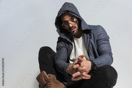 man with hoodie on head holding hands together while sitting