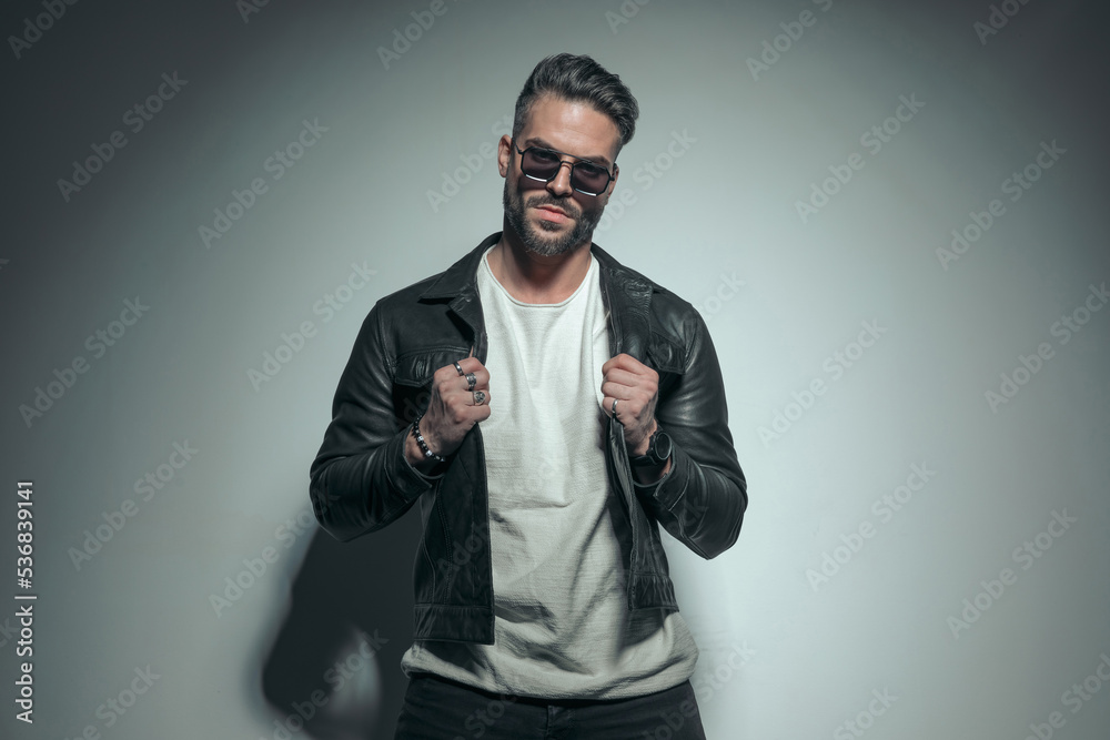 casual man pulling his leather jacket, wearing sunglasses casual man pulling his leather jacket, wearing sunglasses