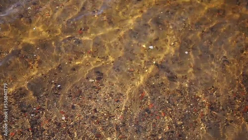 Bronze stones under sun-drenched shallow water, waves in shallow water