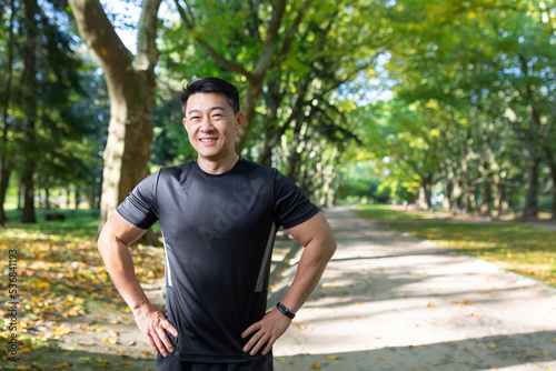 Portrait of Asian athlete in autumn park on sunny day, man in sportswear smiling and looking at camera, fitness instructor before training.