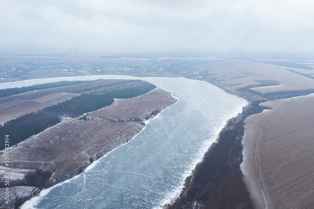 Aerial view of a river covered with ice, severe frosts, rural winter landscape of a winding river and fields