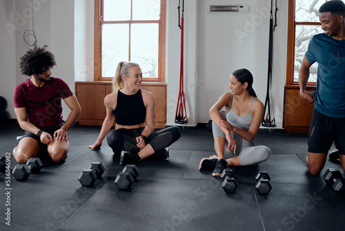 Group of confident multiracial young adults sitting by weights at the gym