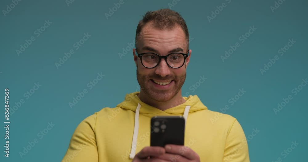 funny guy in yellow shirt holding telephone, writing messages, being playful and foolish, making funny faces and laughing on blue background funny guy in yellow shirt holding telephone, writing messages, being playful and foolish, making funny faces and laughing on blue background