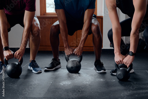 Close-up of three muscular multiracial young adults doing kettlebell squats at the gym