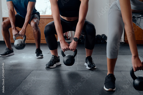Close up of three determined multiracial young adults doing kettlebell squats at the gym