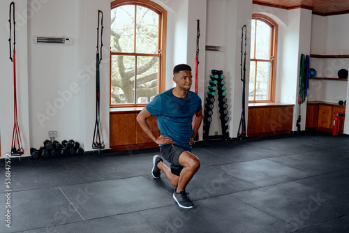 Determined young black man doing lunges with hands on hips at the gym