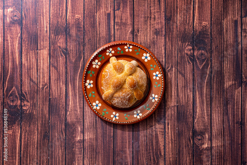 Traditional Mexican bread of the dead also known as "Pan de Muerto" on traditional Mexican tableware on brown wooden background.