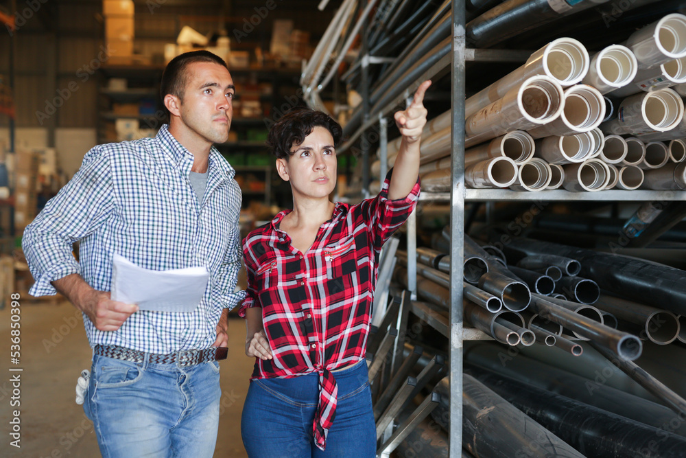 Woman and man having conversation while making stock control, verifying documents and making pointing finger gesture.