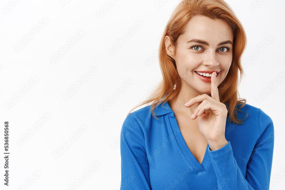 Close up portrait of smiling pretty woman holding finger on lips, shushing, has secret, stands over white background Close up portrait of smiling pretty woman holding finger on lips, shushing, has secret, stands over white background