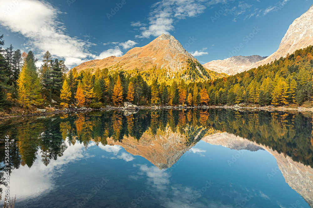 autumn view of Saoseo lake in the Dolomites. Fantasy autumn scene with colorful sky, majestic rocky mountain and colorful trees glowing with sunlight