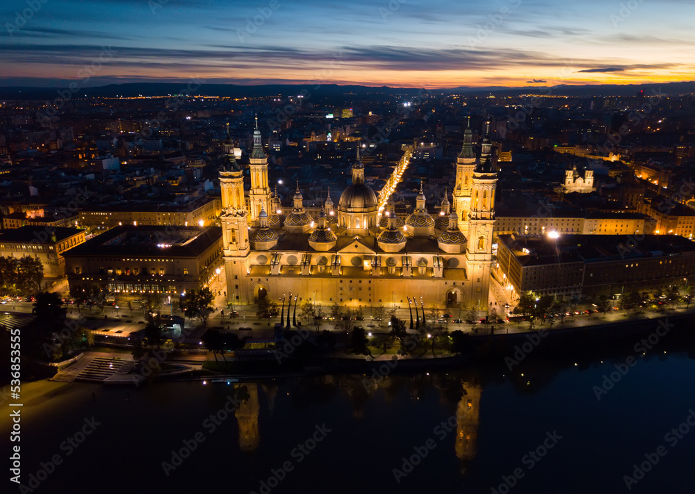 Aerial view of lighted Roman Catholic Basilica Our Lady of Pillar on background of Zaragoza cityscape and Ebro river at dusk, Spain..