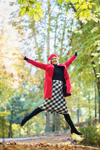 Stylish woman jumping happily in autumn park