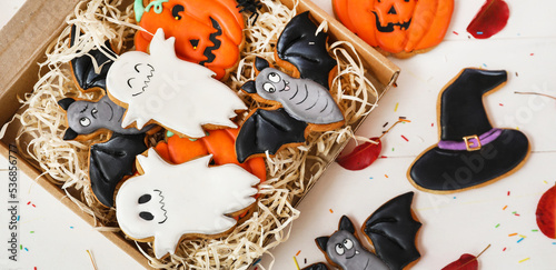 Cardboard box with creative Halloween cookies on white wooden background, top view