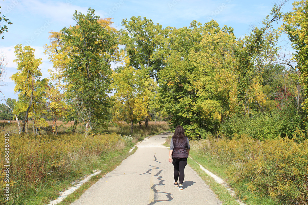 Obraz premium Woman walking in on a trail at Miami Woods in Morton Grove, Illinois in autumn
