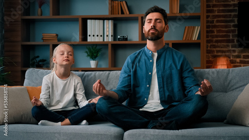 Healthy caucasian family practice yoga together sit in lotus pose young father teach little daughter meditate calm down emotions relaxation exercise good life habit at home during quarantine no stress