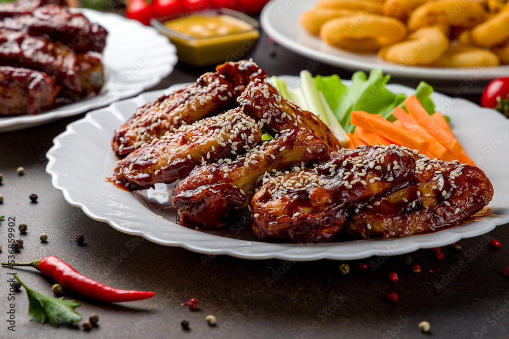 chicken wings in barbecue sauce with sesame on white plate on dark brown table macro close up