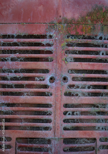Old, rusted tractor grill with spider webs and old red paint