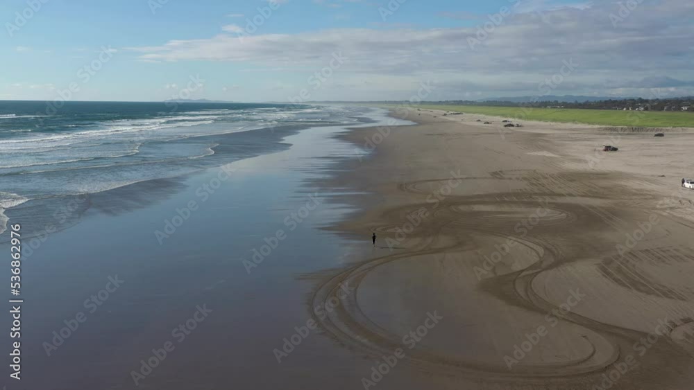 Young man keeps a healthy lifestyle by running at the beach. Aerial drone follow.