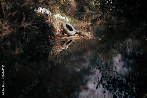 Old Tire and other Garbage Dumped in Waters Polluting a River. Car parts floating in polluted water creating environmental problems
 photo