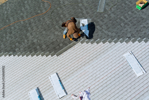 Aerial view of worker nailing new roof shingles with bitumen using an air hammer