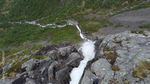 Man standing on edge of dangerous tall cliff with spectacular waterfall - Fjellfossen waterfall in Eidslandet mountain Vaksdal Norway photo