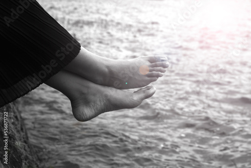 Relax bare feet on the water. Young woman sitting on sea with legs on the water with sun light background in black and white.